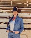 Woman wearing a denim outfit and cowgirl hat in front of a horse trailer