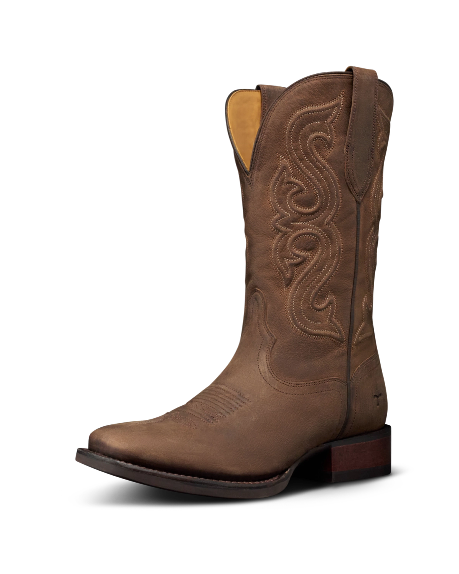 The Tess in Cafe Goat. A single brown leather cowboy boot from The Tess Goat, featuring decorative stitching, a square toe, and a low wooden heel, photographed on a plain white background.