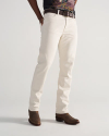 Person wearing off-white jeans, a brown belt, a graphic t-shirt, and brown cowboy boots, standing against a plain light background.