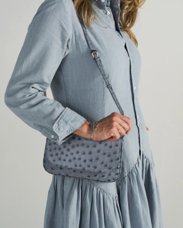 A person in a light blue, long-sleeved dress carries a textured, blue crossbody bag with a strap over their shoulder.