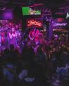 A live band performs on stage in a crowded bar with neon signs and a focused audience enjoying the music.