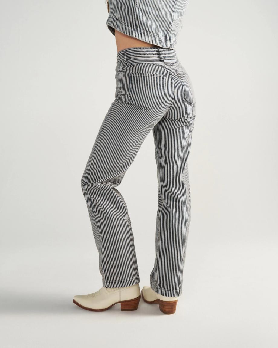 Person wearing striped pants, a matching jacket, and white heeled boots, standing sideways against a plain background.