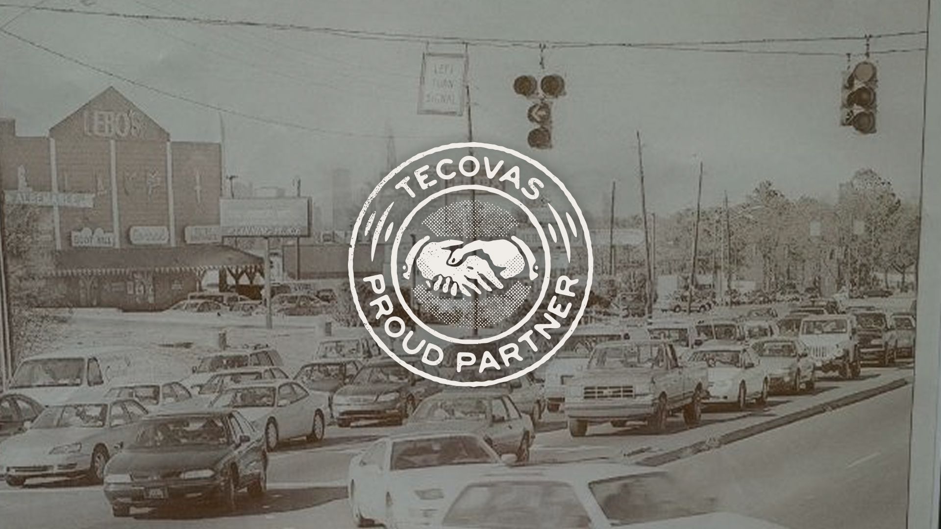 Vintage photo of a busy street with traffic, overlaid by a white circular "Tecovas Proud Partner" logo featuring a handshake.