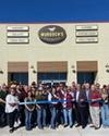 A group of people stands in front of a Murdoch's Ranch & Home Supply store, holding a large ribbon for a ribbon-cutting ceremony.