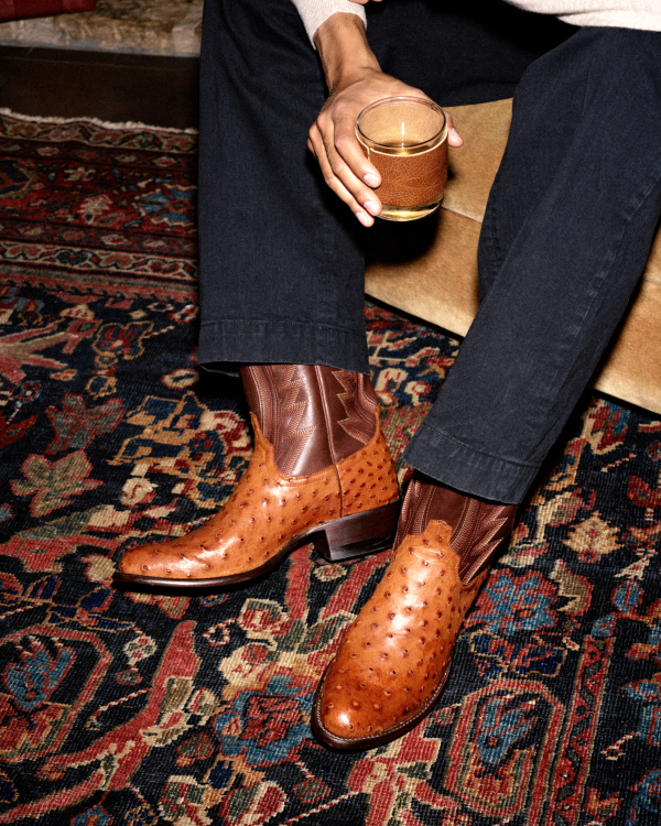 The Wyatt in Pecan Ostrich. Person wearing dark trousers and brown Pecan Ostrich cowboy boots, holding a glass.