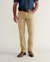 A person wearing a blue denim shirt, tan pants, brown belt, and brown boots stands against a plain background with one hand in their pocket.