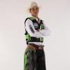 Man in a cowboy hat, white shirt, protective vest, and chaps with green designs stands with arms crossed against a plain background.