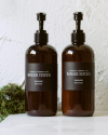 Two brown pump bottles with black labels stand on a counter. The labels read "Ranger Station Oakmoss Hand Wash" and "Ranger Station Oakmoss Hand Cream." Moss is visible to the left of the bottles.