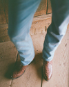 Person wearing light blue jeans and brown leather cowboy boots standing on a wooden floor.