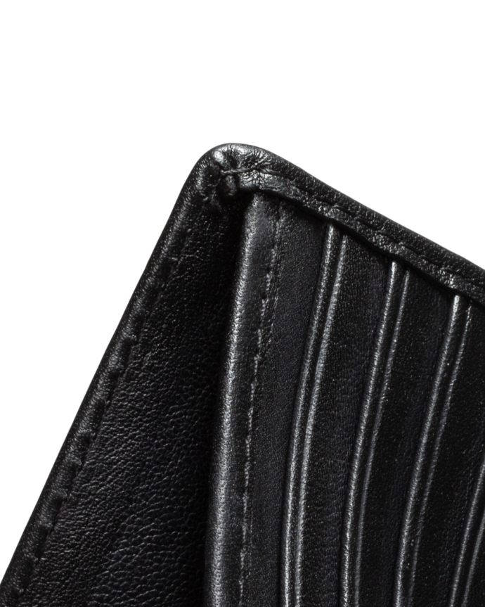 Close-up of a black leather wallet corner, showing stitching and vertical grooves, against a black background.