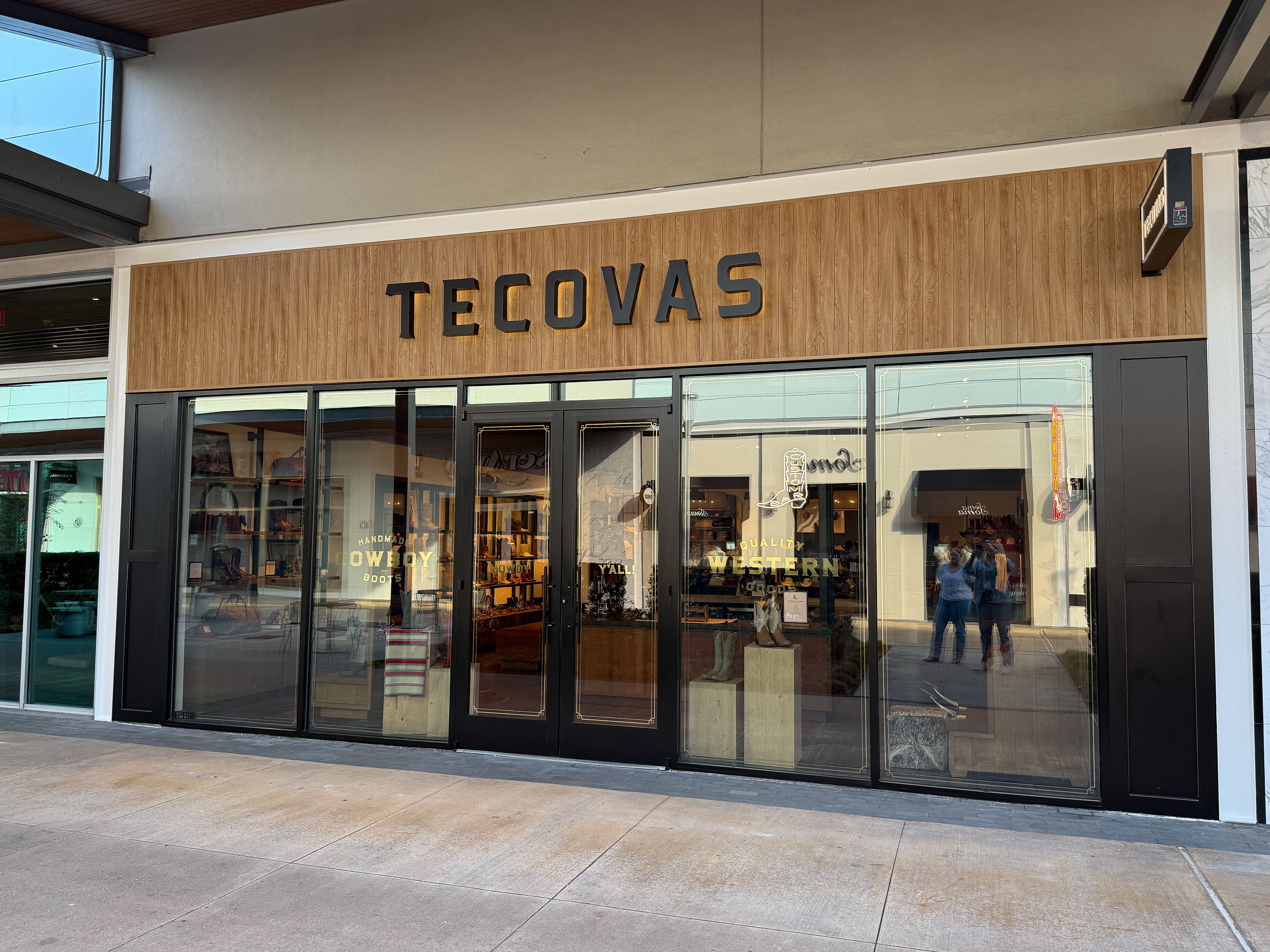 The storefront of Tecovas, a retail store with large glass windows and wooden accents, displaying boots and western apparel inside.