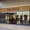 The storefront of Tecovas, a retail store with large glass windows and wooden accents, displaying boots and western apparel inside.