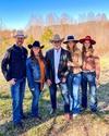 Five people wearing cowboy hats standing outdoors on grass with trees in the background.