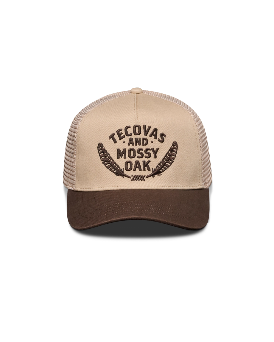 A tan and brown trucker hat with "Tecovas and Mossy Oak" and feather graphics embroidered on the front.