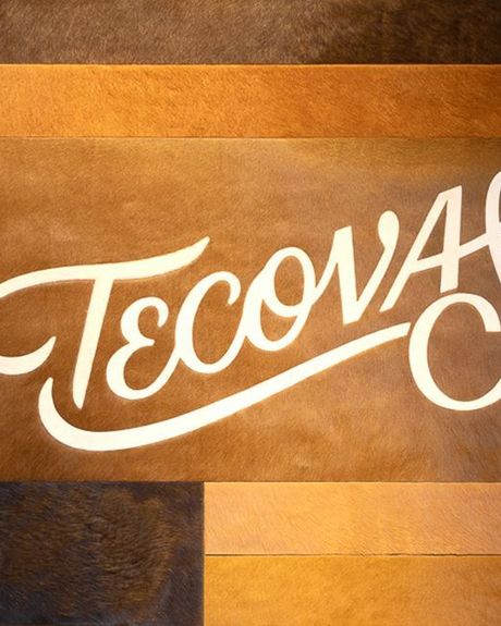 The image shows the word "Tecovas" in cursive, displayed on a background of various brown leather patches.