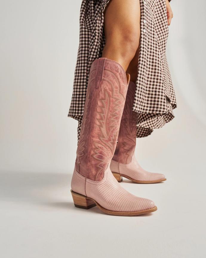 Person wearing pink cowboy boots and a brown gingham skirt, standing on a light-colored surface.