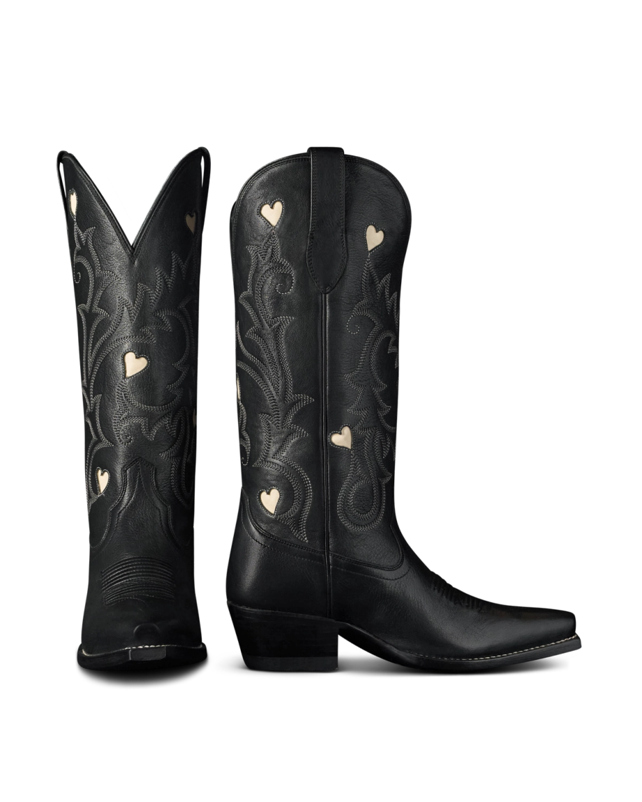 The Annie in Midnight Cowhide. A pair of black midnight cowhide cowboy boots with decorative stitching and small heart-shaped cutouts, shown from the front and side against a white background.