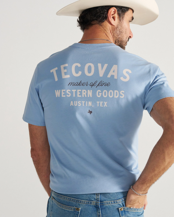 Man wearing a light blue T-shirt and cowboy hat, seen from the back. The T-shirt reads, "Tecovas maker of fine Western Goods Austin, Tex.
