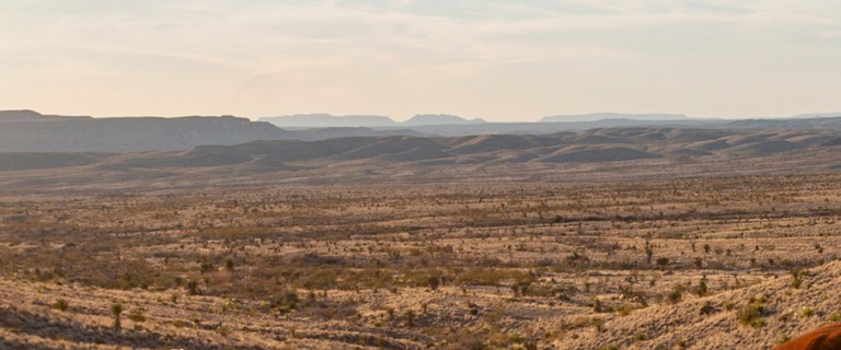 Desert landscape with two people in cowboy hats riding horses during sunset