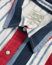 Close-up of a collared shirt with vertical red, white, and blue stripes, snap buttons, and a sewn label that reads "Genuine Western Goods, Modern Fit.