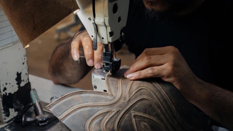 Person using an industrial sewing machine to stitch a detailed pattern onto a piece of brown leather.