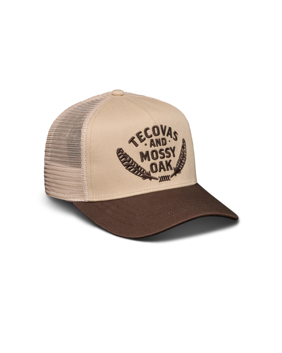 A beige and brown trucker hat with mesh back, featuring "Tecovas and Mossy Oak" text and two feather graphics on the front.