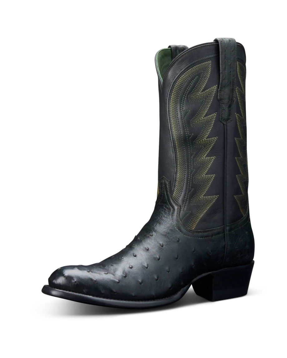 A single black cowboy boot with decorative stitching and a short heel, set against a black background.