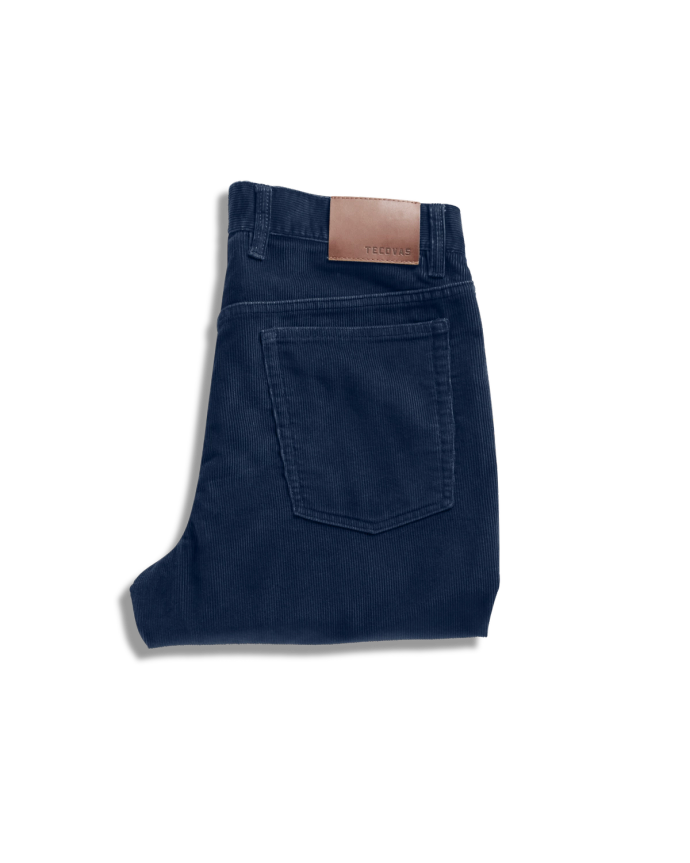 A pair of folded dark blue corduroy pants with a brown leather patch on the waistband, displayed on a light background.