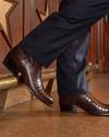 Man leaning against a wall wearing the Tecovas crocodile boots, the Marshall.