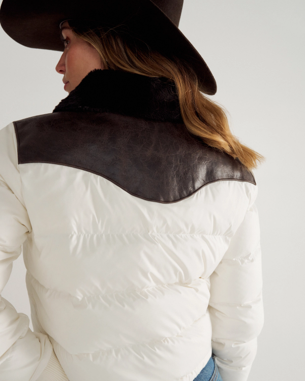 Person in a white puffer jacket with a dark brown yoke and collar, wearing a dark cowboy hat, shown from the back against a plain background.