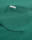 Close-up of a green fabric shirt pocket with a small white label that reads "Tecovas" sewn along the top edge of the pocket.