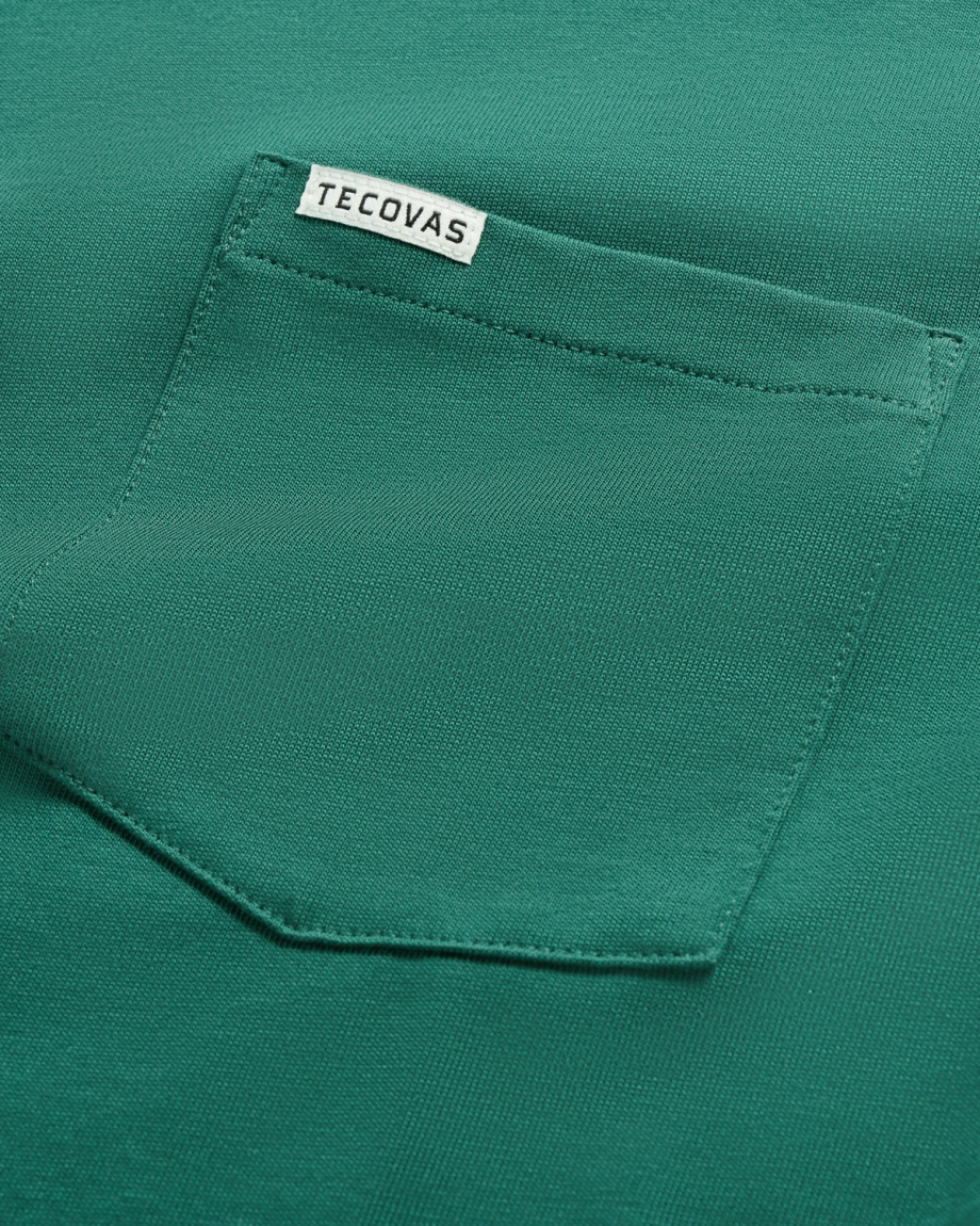 Close-up of a green fabric shirt pocket with a small white label that reads "Tecovas" sewn along the top edge of the pocket.