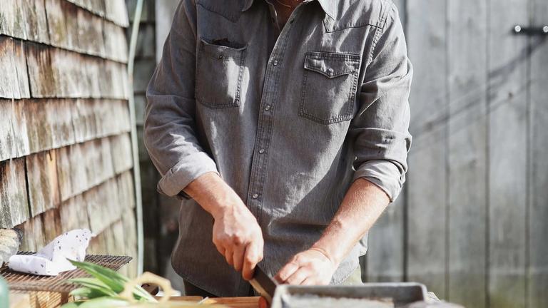 Chef Brad Leone wearing a denim pearl snap cooking outdoors. 