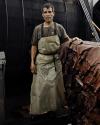 A man wearing a protective apron stands beside a large stack of brown leather hides inside an industrial facility.