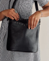 A person wearing a black-and-white checkered dress holds a black leather handbag with metal studs, accessorized with a large ring and a bracelet.