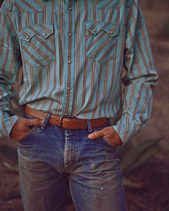 Person wearing a blue-striped, long-sleeve shirt and jeans, hands in pockets, standing outdoors.