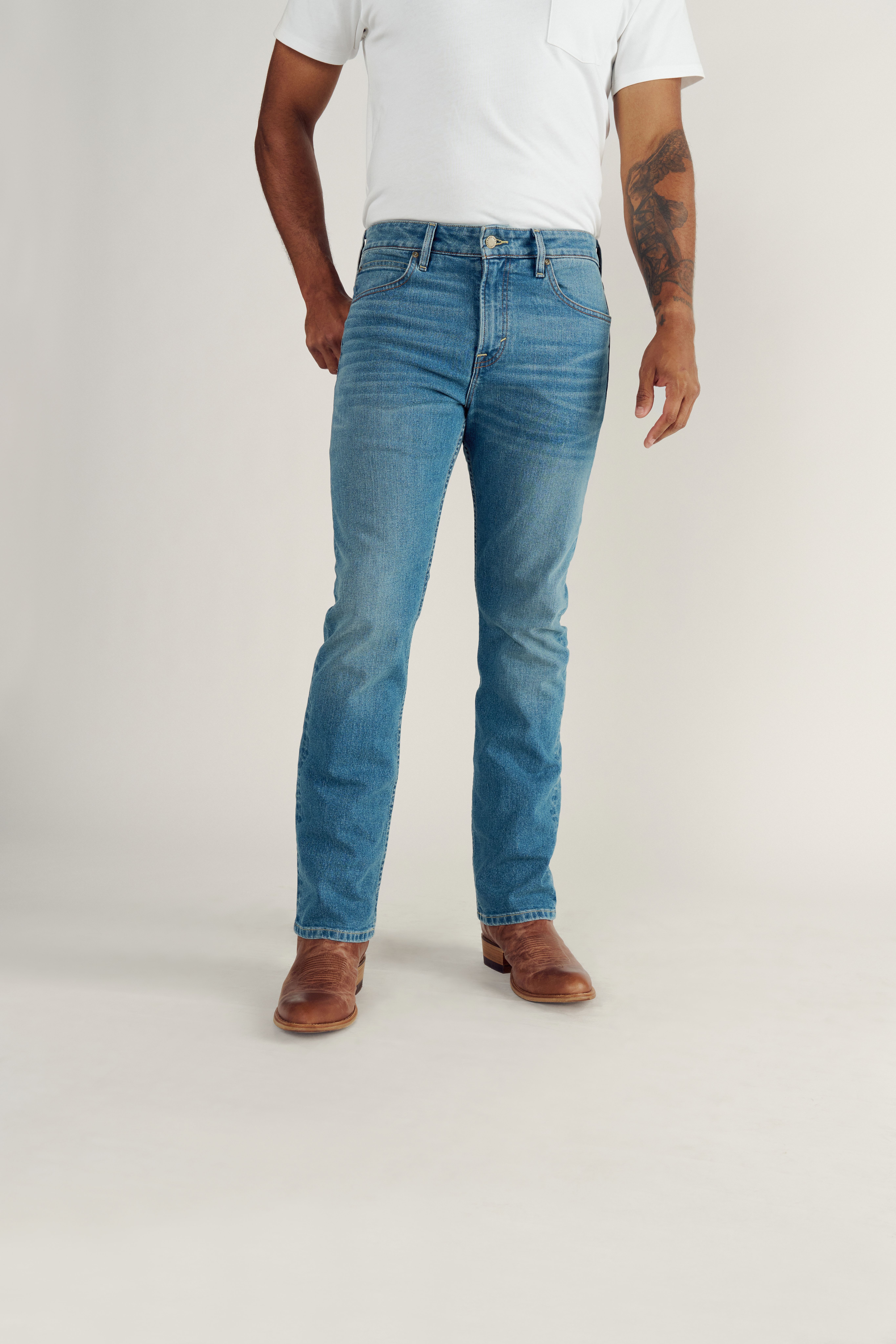 A person wearing a white t-shirt, blue jeans, and brown boots stands against a plain background.