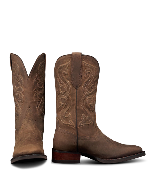 The Tess in Cafe Goat. A pair of brown leather cowboy boots with decorative stitching, inspired by The Tess Goat, one boot standing upright and the other displaying the front view.