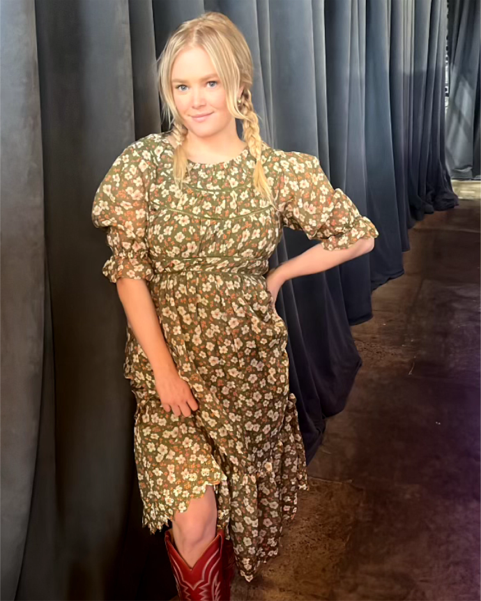 A blonde woman in a floral dress and cowboy boots.