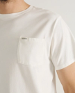 A person wearing a white T-shirt with a chest pocket that has "Tecovas" printed on it.