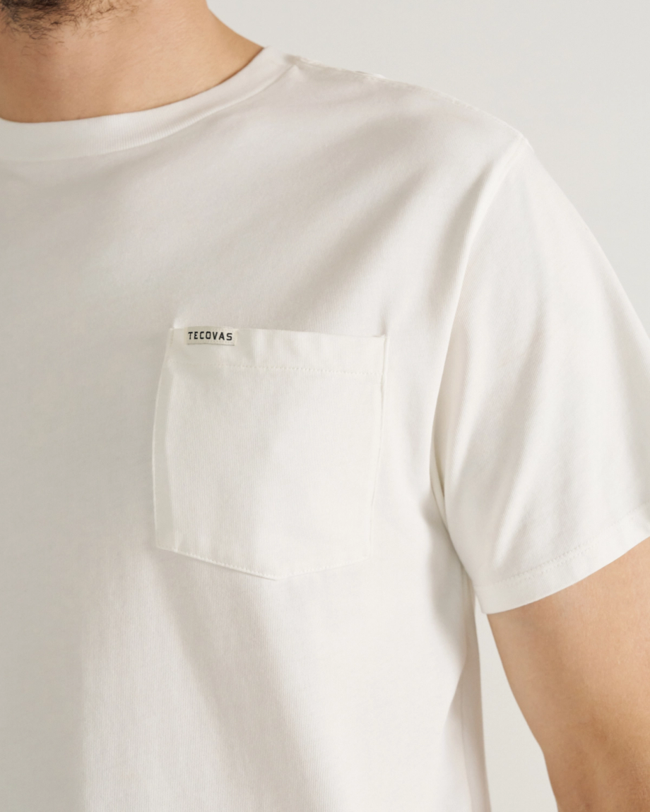 A person wearing a white T-shirt with a chest pocket that has "Tecovas" printed on it.