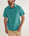 Man wearing a teal short-sleeve button-up shirt with two pockets, paired with beige pants.