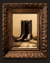 A pair of black cowboy boots displayed in the center, reflected in an ornate, rustic wooden frame.
