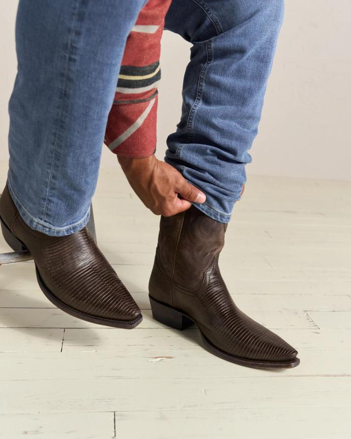 Person wearing brown cowboy boots with blue jeans, adjusting the fit while seated.