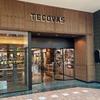The entrance to a Tecovas store in a mall, featuring wood paneling, glass doors, and displays of boots and leather goods inside.
