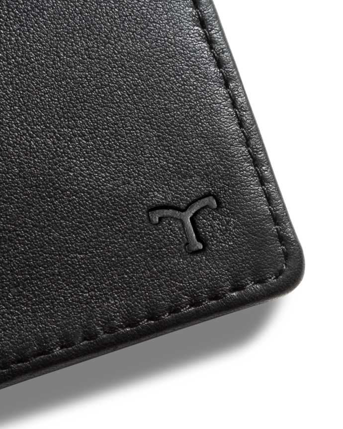 Close-up of a black leather wallet corner with an embossed "T" logo.