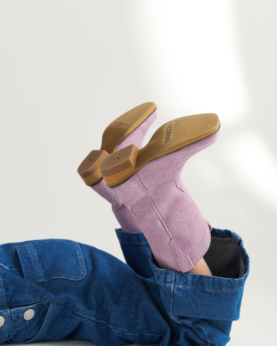 A person wearing denim pants and light purple heeled boots with tan soles is lying down with their legs raised.