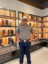 A man in a cowboy hat standing in front of shelves of cowboy boots.