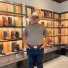 A man in a cowboy hat standing in front of shelves of cowboy boots.