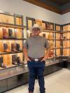 A man in a cowboy hat standing in front of shelves of cowboy boots.
